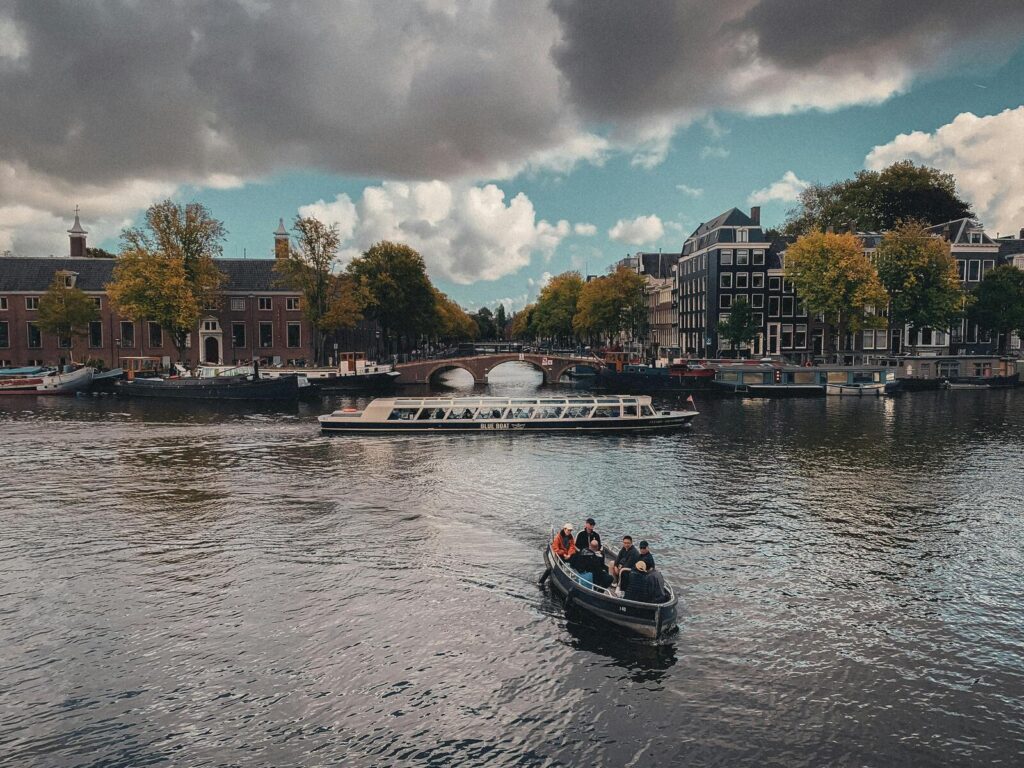 Boot met mensen vaart over Amsterdamse gracht met brug en gebouwen op de achtergrond