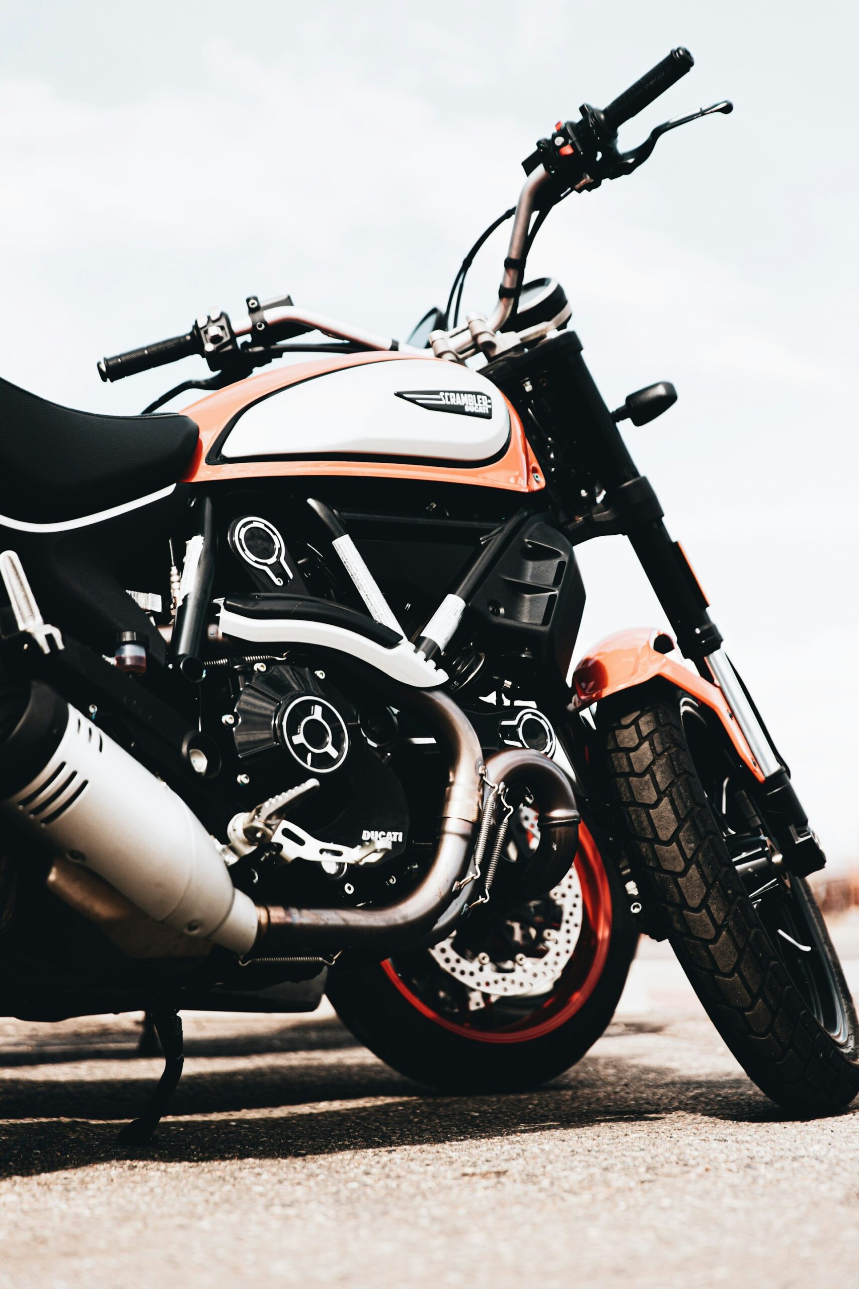 Ducati Scrambler motor met oranje-witte tank en zwarte uitlaat, geparkeerd buiten